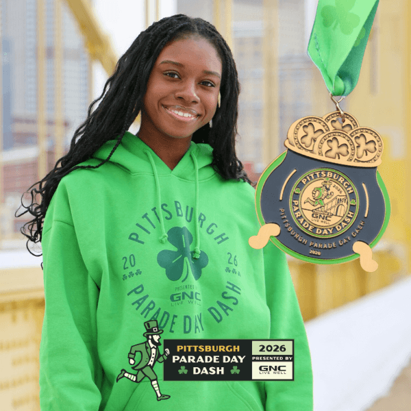 Smiling person in a green hoodie with "Pittsburgh Parade Day Dash" logo, stands on a bridge. A medal with a green ribbon is prominently displayed. Festive and cheerful.